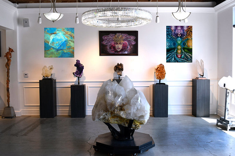   art gallery with large crystal in foreground. In the background, there are three psychedelic paintings. along the back wall are 5 dark wooden pedestals with large geodes or crystals displayed on them
