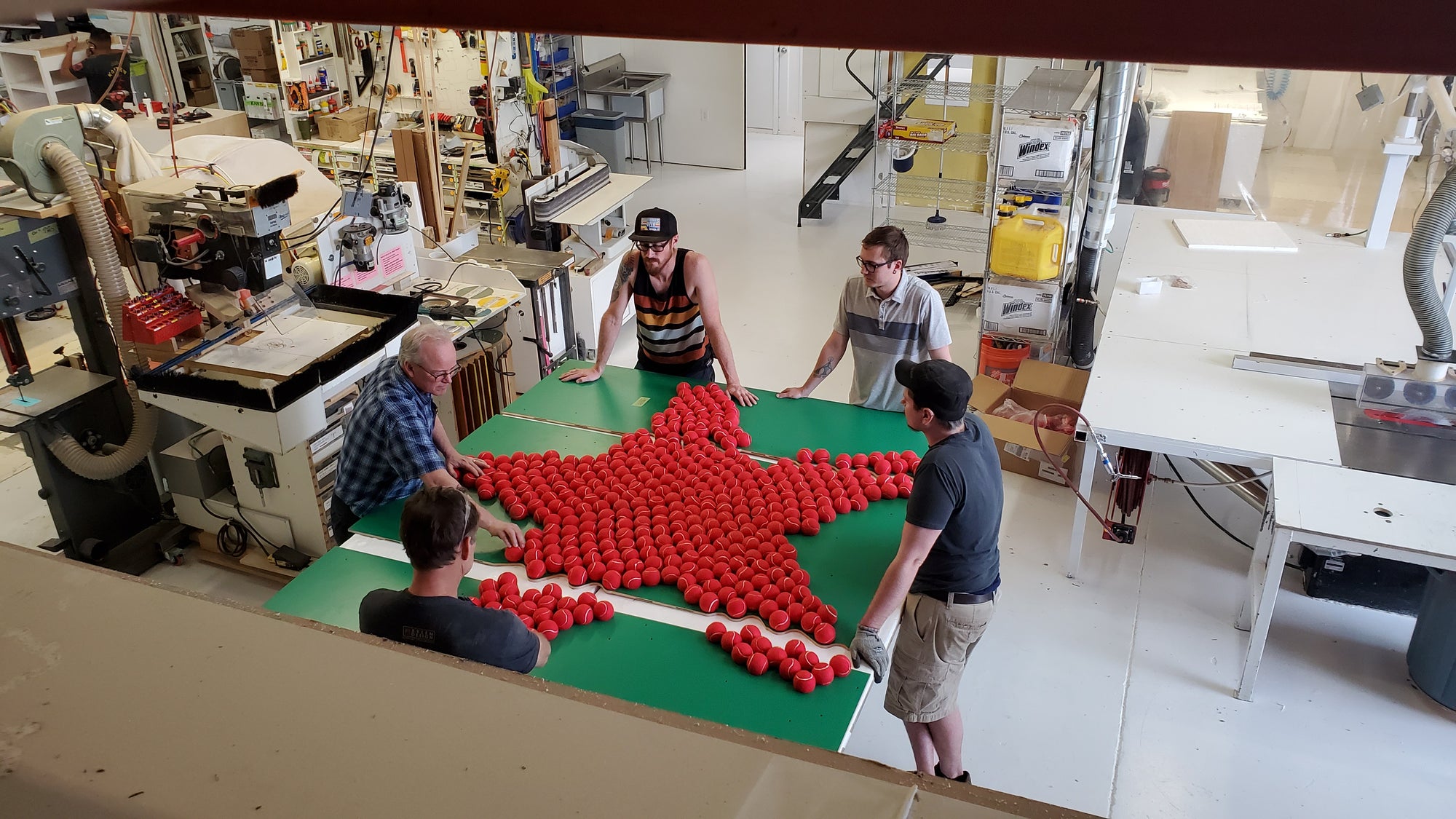 five men in manufacturing warehouse standing around a custom made heineken display. you see the green background with the bright red star.