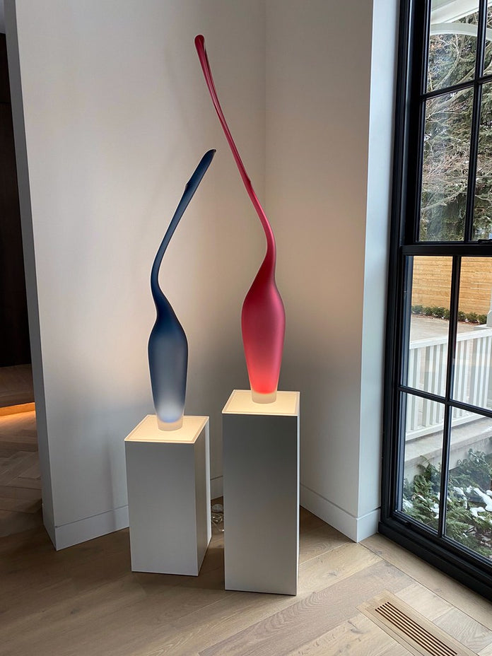 Two white laminate pedestals with ambient lighting. There are abstract sculptures on them.