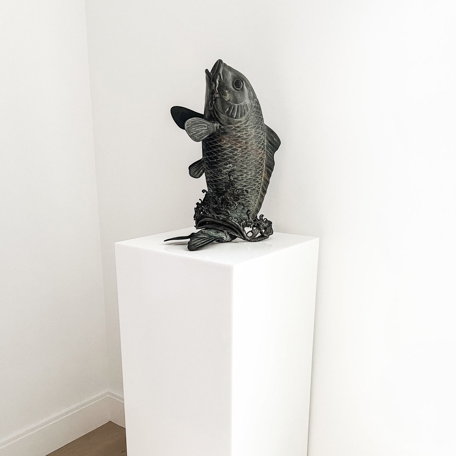 White acrylic pedestal with bronze cast fish sculpture.