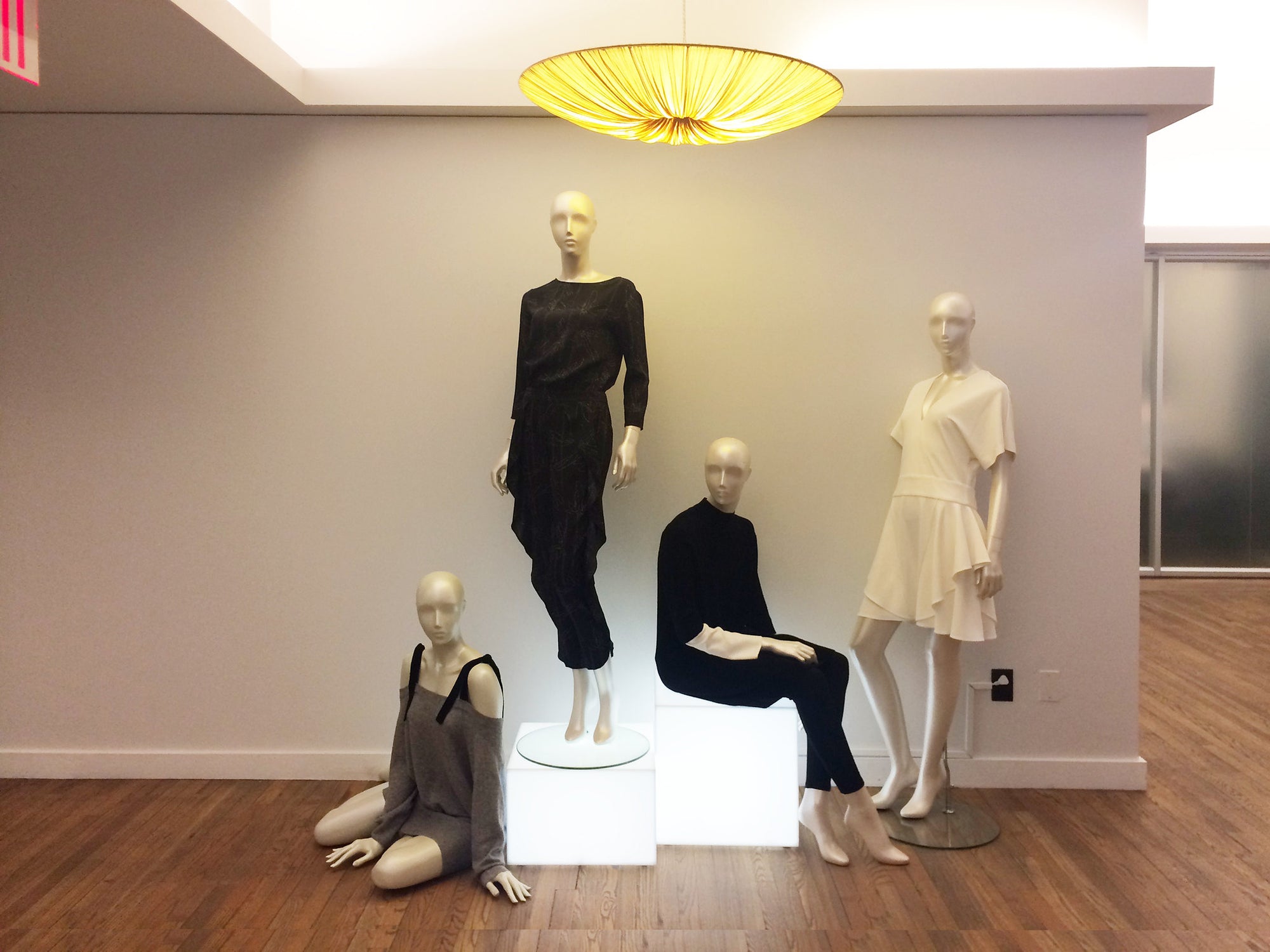 Four mannequins seated on and around two sign white illuminated cube pedestals.