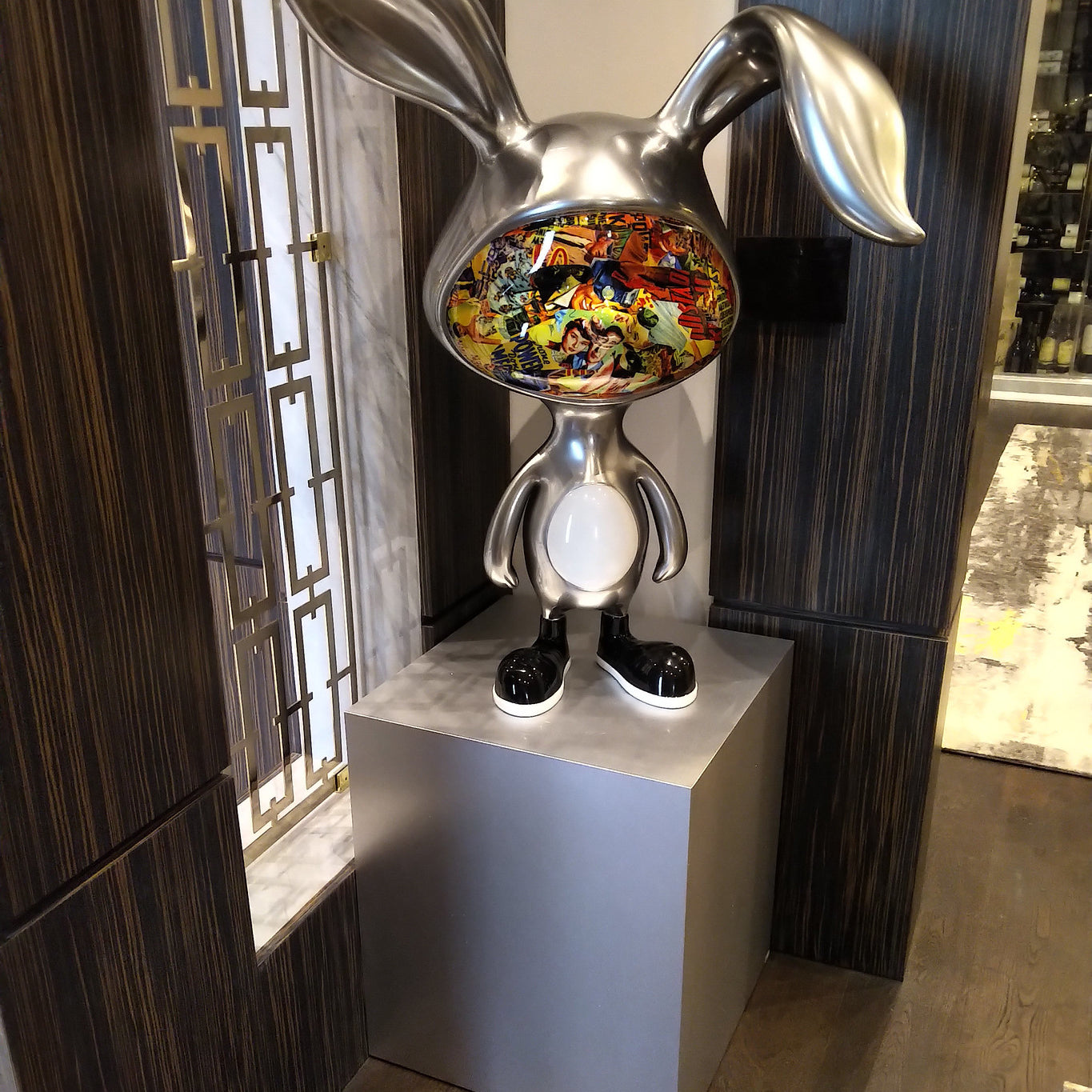 Silver brushed aluminum pedestal with sculpture of metal rabbit on top.