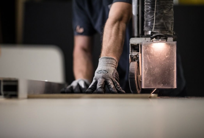 close up of a person using a bandsaw. you can only see their hands and arms. they are wearing work gloves.